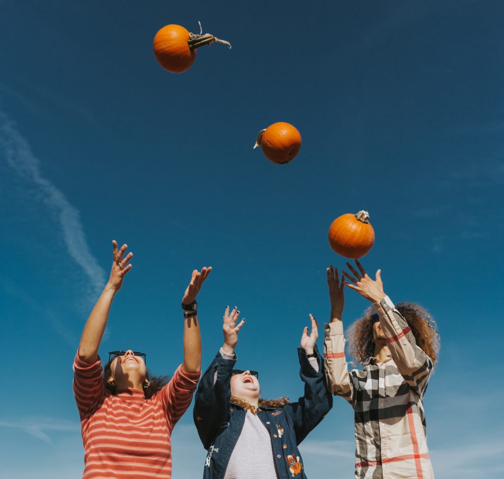 Three friends throwing small pumpkins up in the air